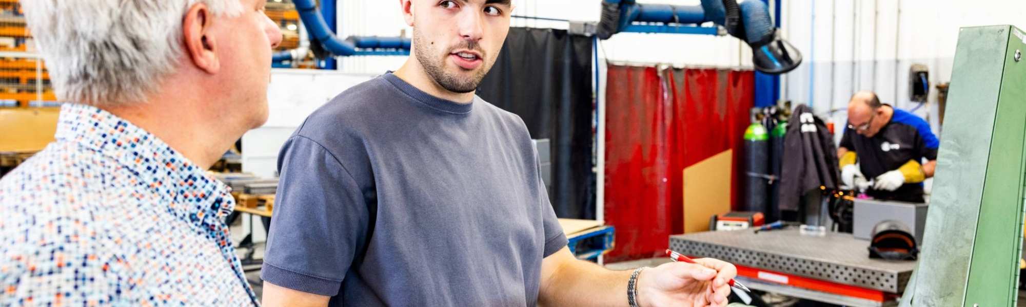 Technische Bedrijfskunde student overlegt met stagebegeleider bij machine.