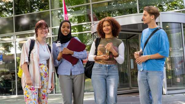 Vier studenten staan bij gebouw LvS10 bij draaideur, buiten. Op een rijtje. 