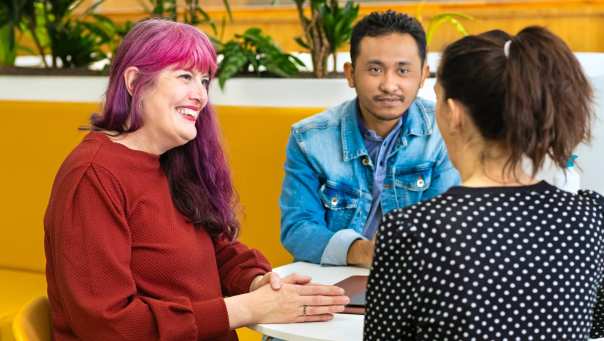 3 studenten Leraar Engels praten met elkaar aan een tafel.