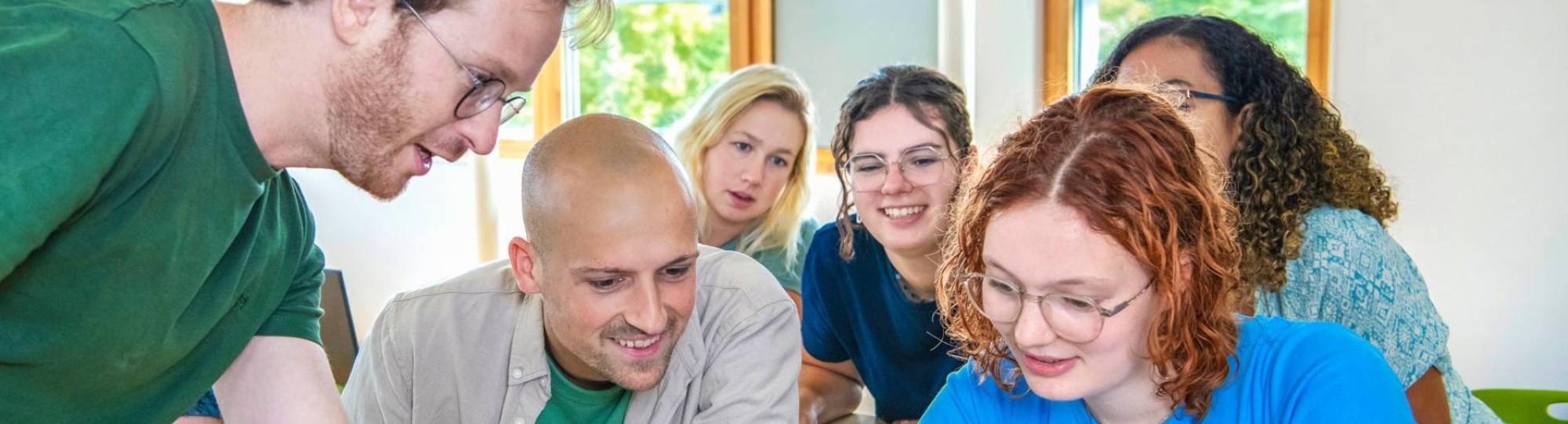 Leraar Wiskunde wijst iets aan op de laptop en klas kijkt van achter nieuwsgierig mee
