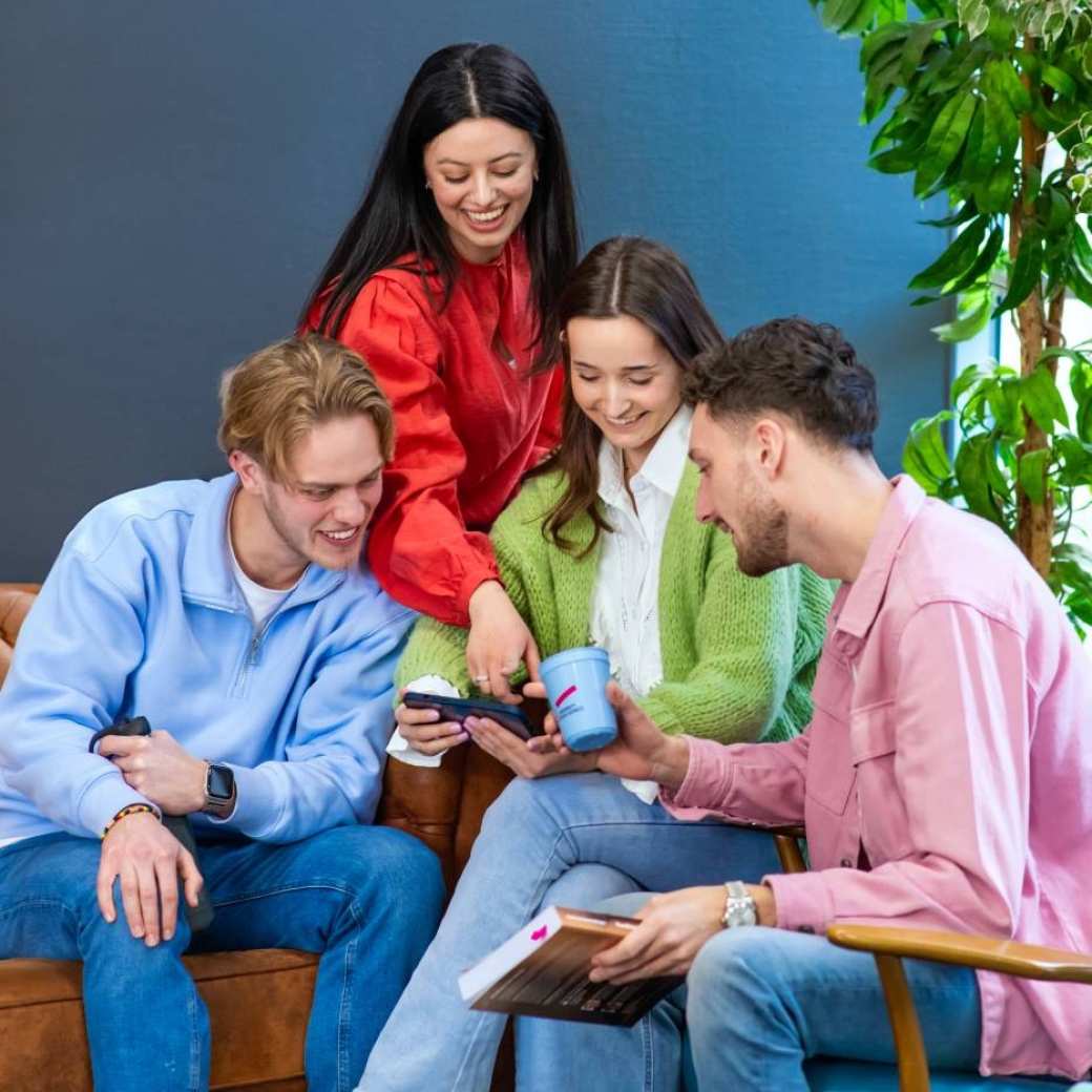 Vier studenten zitten in de kantine en kijken lachend naar de telefoon die ze in hun handen hebben