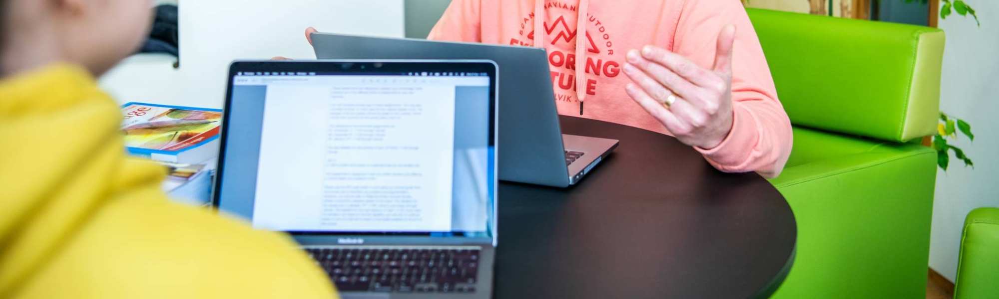 Foto Master Academie Educatie. 2 masterstudenten zitten aan een tafeltje op Kapittelweg 35 met hun laptops tegenover elkaar. Een van hen legt wat uit aan de ander.