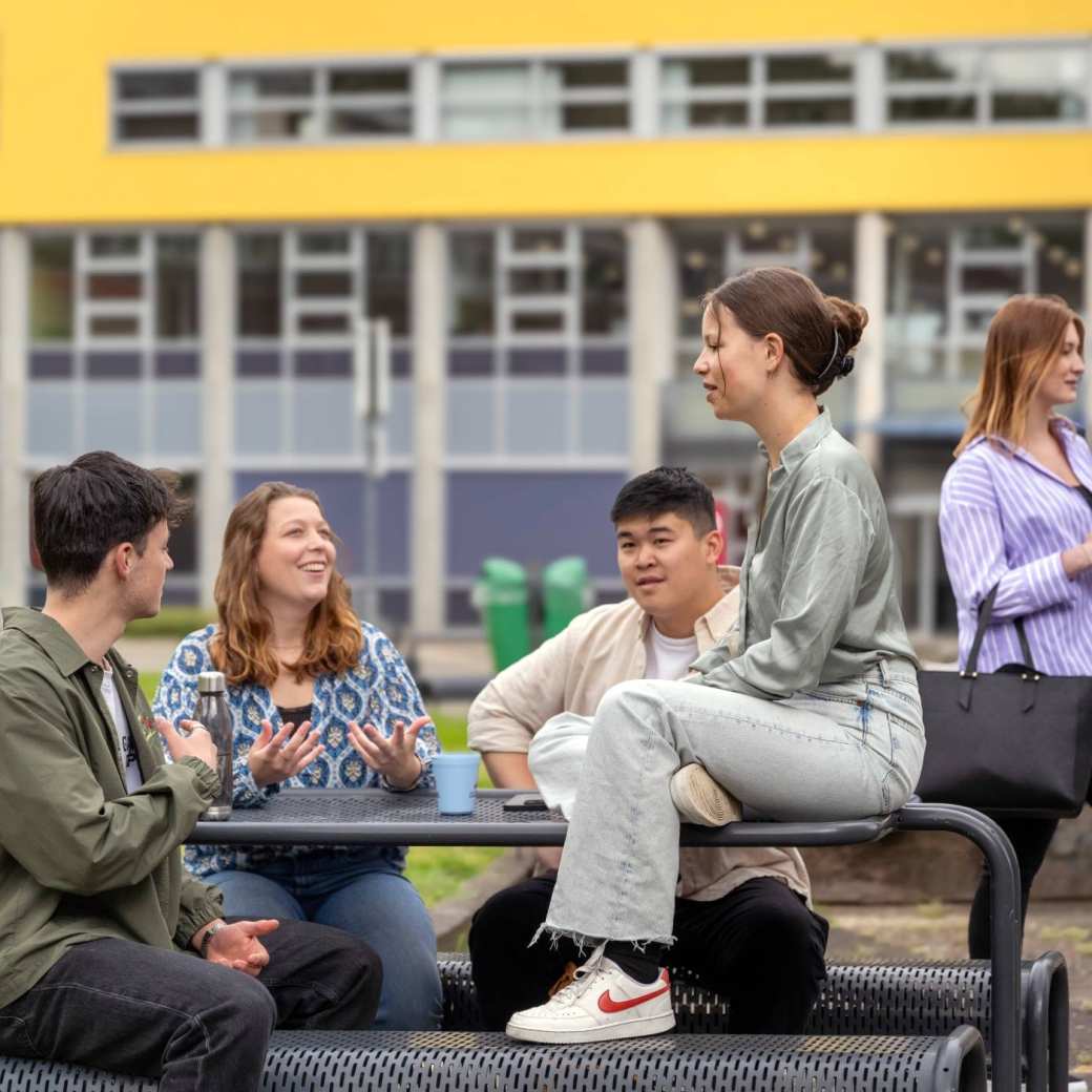 Groepje studenten zitten buiten aan de picknicktafel, op de campus Arnhem.