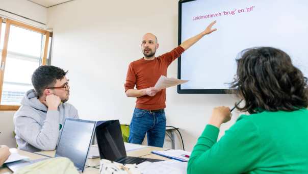 Docent Leraar Nederlands wijst iets aan op het scherm tijdens de les.