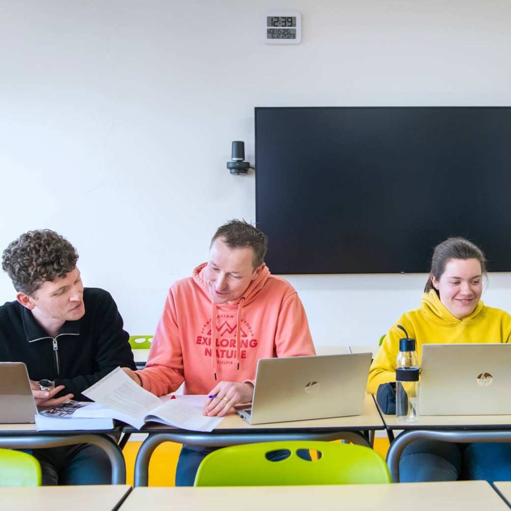 Foto Master Academie Educatie. 4 masterstudenten zitten geconcentreerd op een rij achter hun laptops aan een tafel.
