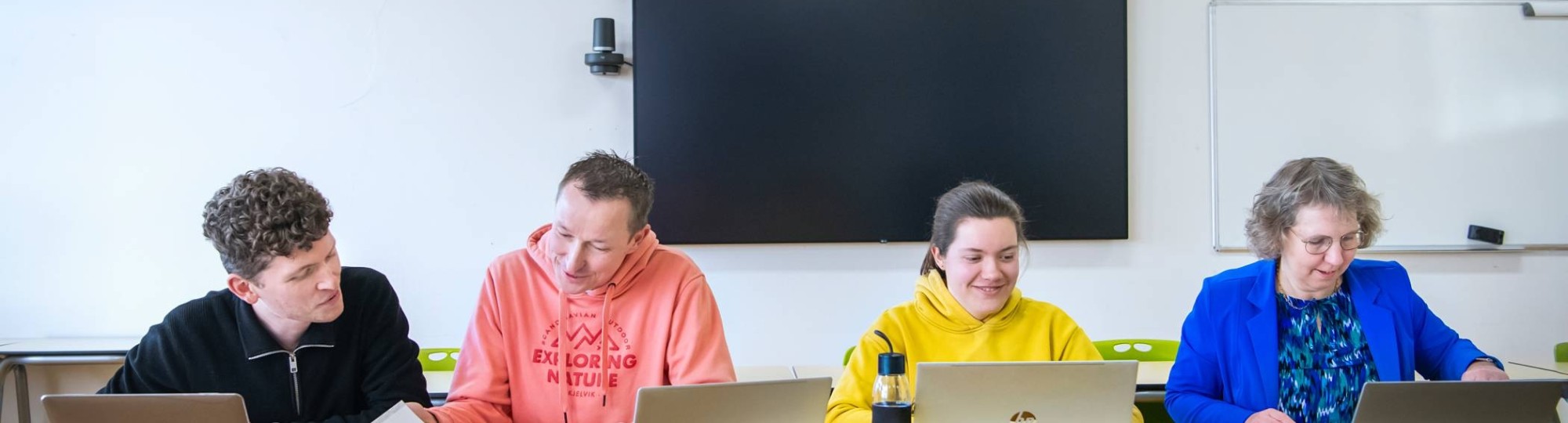 Foto Master Academie Educatie. 4 masterstudenten zitten geconcentreerd op een rij achter hun laptops aan een tafel.