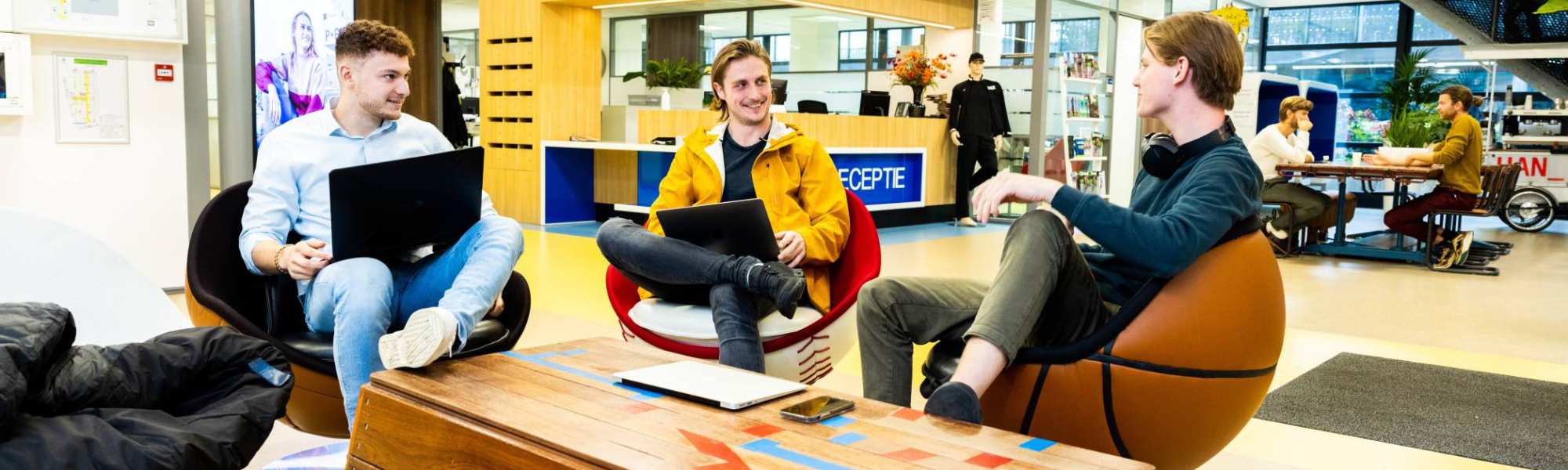 Stagiairs kletsen op draaistoelen in hal Gymnasion.