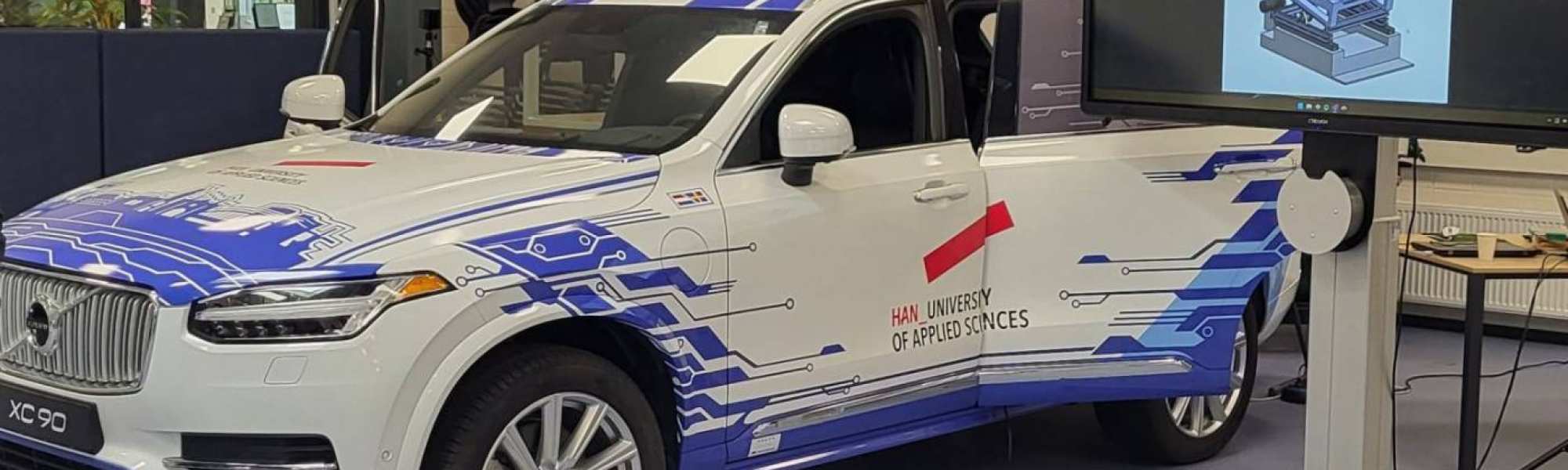 Volvo XC90 die opvallend is gewrapt in een passende lichtblauwe kleurstelling en bijpassend HAN design. 

Deze Volvo XC90 wordt o.a. gebruikt voor het project HUBRIS (HUman-like Behaviour of Robotic In-vehicle Systems). Hierin zal de stoel van de bijrijder aangepast worden om als een rijsimulator de passagier het gevoel te geven dat deze echt meerijdt. Met een VR-bril op zal de testpersoon virtueel de A50 van Arnhem naar Apeldoorn (mee)rijden. Soms bestuurt door een normale 'autopilot', soms door een 'robotbestuurder' die meer mensachtig gedrag vertoont. 

Het doel is uit te vinden of onze mensachtige robot voor de passagier fijner aanvoelt dan de standaardsystemen.