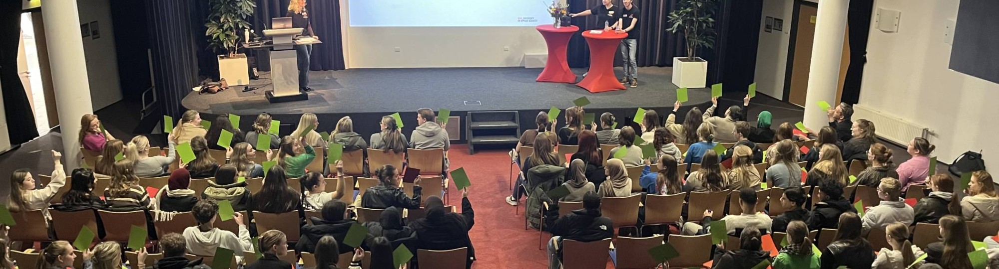 Foto's van de plenaire sessie met mbo-scholieren die groene kaartjes omhoog houden, voor de mbo-hbo proefstudeermiddag van Educatie en Mens en Maatschappij op 7 maart 2024