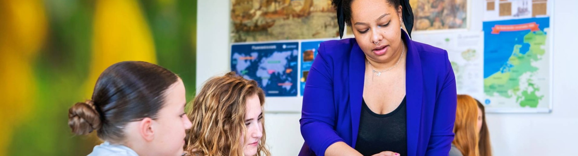 Angel Olatunji geeft staand uitleg bij een tafel met 2 middelbare scholieren van het Citadel College.