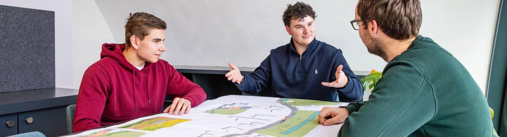 drie mannen in een overlegsituatie met een omgevingskaart op de overlegtafel