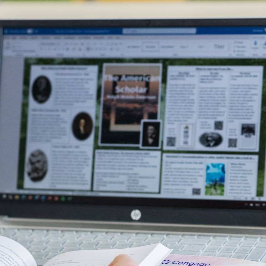 Foto Master Academie Educatie. Een masterstudent zit achter haar laptop met een boek opengeslagen in haar handen.