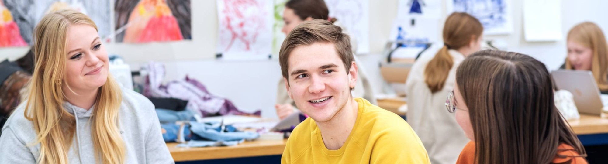 Fotoshoot maakdagen beeldende vorming 2022.Drie studenten met elkaar in overkeg tijdens de les beeldende vorming. De jongen in het midden lacht