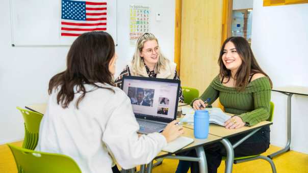 3 cursisten Engels: Cambridge Advanced C1 werken in een lokaal met een Amerikaanse vlag aan de muur.