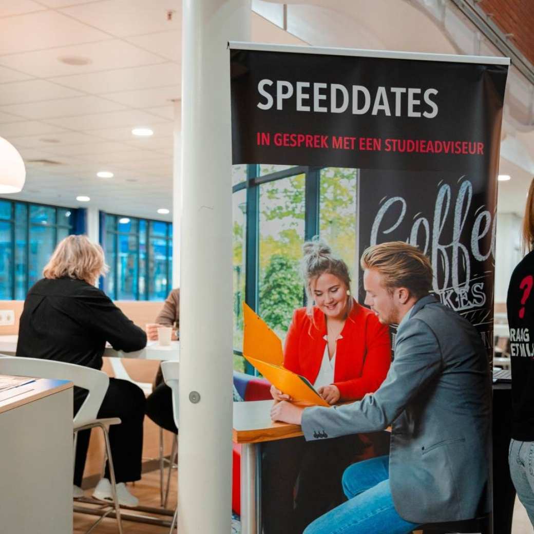 Adviseur achter een tafel op de open avond van de associate degree Commerciële Economie deeltijd