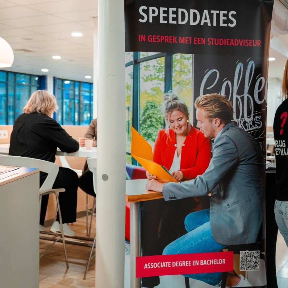 Adviseur achter een tafel op de open avond van de associate degree Commerciële Economie deeltijd