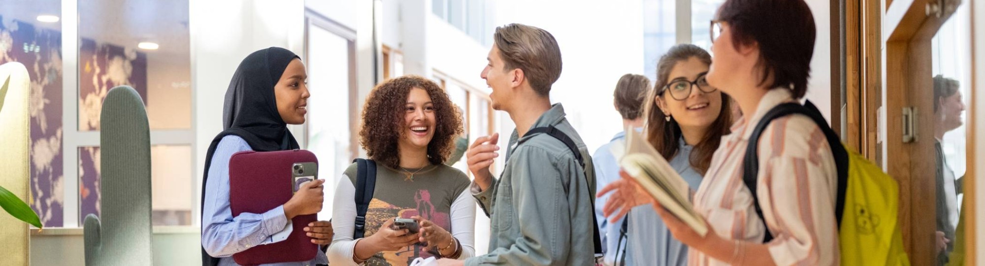 Een groepje studenten staan te wachten voor de klas en hebben plezier. 